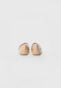 Sapatilhas de verniz bege com bico arredondado, design minimalista, tira fina ao tornozelo e textura suave. Sola plana para maior conforto.