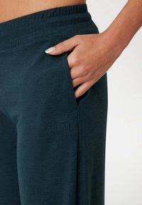 Tirkizne trenirke od mekog materijala s rastezljivim pojasom, s bočnom džepom i utisnutim 'GUESS' logom na lijevom bedru.