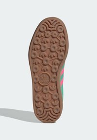 Gummisneakersula med cirkulära och blommiga greppmönster. Främst tan med rosa och gröna accenter på sidorna. Hållbar textur, atletisk design.