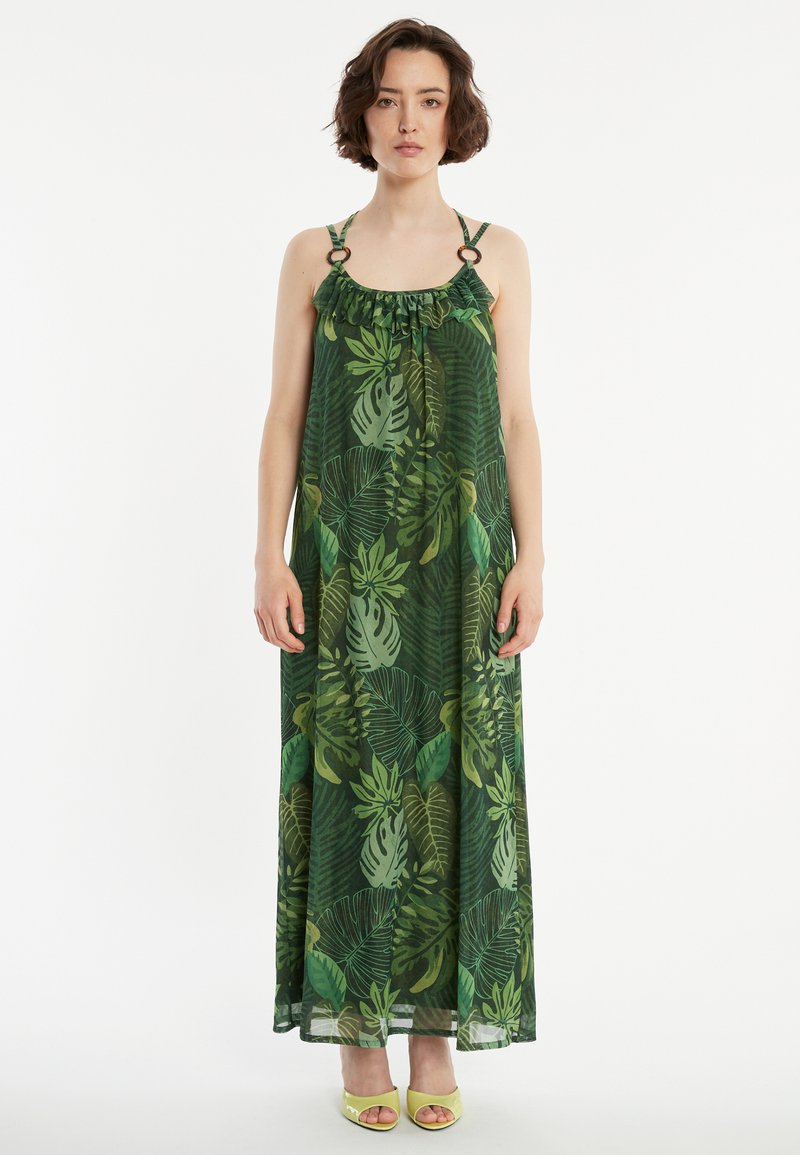 Maxikleid mit grünen Blattmustern, leichtem Stoff, rüschigem Halsausschnitt und großen Ringen an den Schulterträgern. Getragen mit gelben Absätzen.
