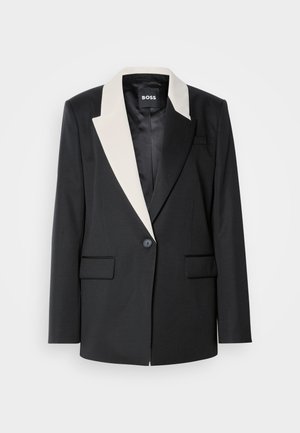 Schwarzer maßgeschneiderter Blazer mit einem kontrastierenden weißen Schalkragen, einem einzelnen Knopfverschluss und zwei Fronttaschen. Glatte Stoffstruktur.