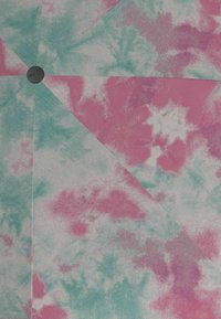 Tela de teñido anudado en colores rosa y verde azulado con pliegues geométricos y una pequeña etiqueta redonda negra adjunta cerca de la esquina superior izquierda.