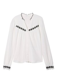 Chemise blanche à manches longues avec un col à volants, ornée d'un bandeau brodé de fleurs noires sur la poitrine et d'accents en dentelle sur les manches.