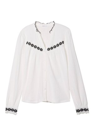 Witte langemouwblouse met een geruffelde kraag, voorzien van een zwarte, geborduurde bloemenband over de borst en kanten accenten op de mouwen.