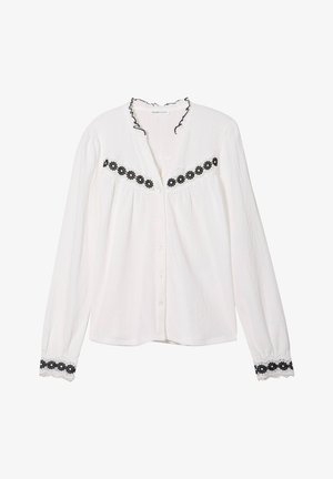 Chemise blanche à manches longues avec un col à volants, ornée d'un bandeau brodé de fleurs noires sur la poitrine et d'accents en dentelle sur les manches.