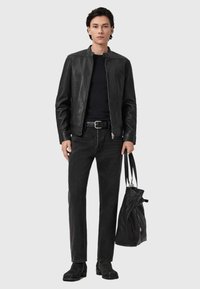 Zwarte leren jack met een staande kraag, aansluitend zwart shirt, donkere spijkerbroek, zwarte riem en enkelboots. Draagt een gestructureerde zwarte tas.