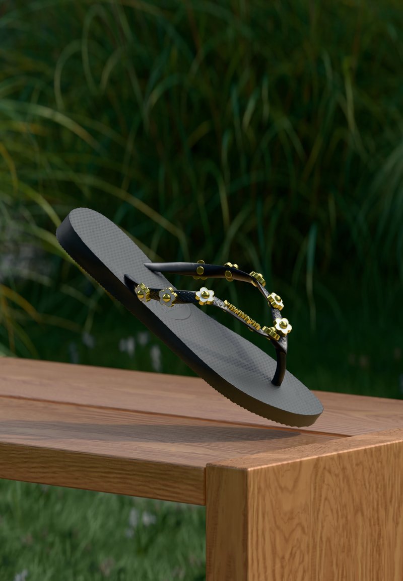 Μαύρο σαγιονάρι με διακοσμητικά χρυσά λουλούδια να αιωρείται πάνω από ένα ξύλινο υπαίθριο τραπέζι, με πράσινο φύλλωμα στο φόντο.