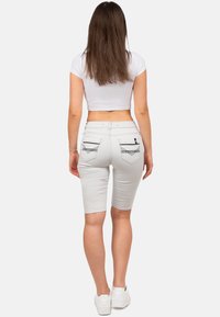 Top bianco corto, pantaloni biker grigi chiari con design a cinque tasche, cuciture decorative sulle tasche posteriori, abbinati a sneakers bianche.