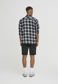 Svart og hvit rutete skjorte med oppbrettede ermer, satt sammen med svarte shorts. Modellen har på seg hvite sokker og grå sko, sett fra baksiden.
