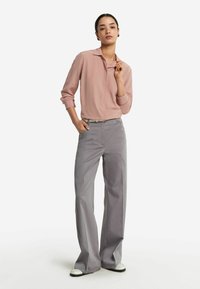 Rosa Bluse mit Kragen und langen Ärmeln, kombiniert mit hellgrauen weiten Hosen, die eine glatte Textur und ein minimalistisches Design aufweisen.