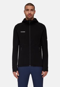 Black fleece jacket with a zip front, high collar, and hood. Features side zip pockets and contrasting stitching. Logo displayed on chest.