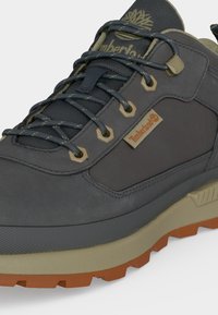 Σκούρο γκρι πεζοπορικό παπούτσι Timberland με μπεζ λεπτομέρειες, μαύρα και γκρι κορδόνια και ανθεκτική καφέ σόλα.