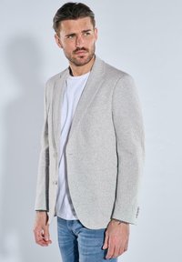 Light gray textured blazer with a single button closure, notch lapels, and two pockets, worn over a white t-shirt and blue jeans.