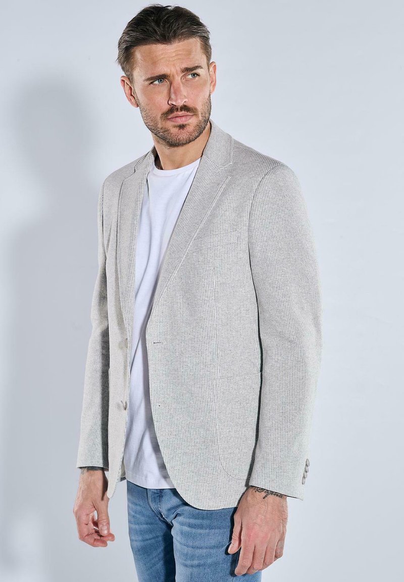 Light gray textured blazer with a single button closure, notch lapels, and two pockets, worn over a white t-shirt and blue jeans.
