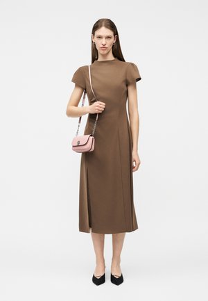 Nainen pukeutuneena ruskeaan midi-mekkoon, jossa on lyhyet hihat, pitäen pientä vaaleanpunaista olkalaukkua ja pukeutuneena mustiin, kärjestä teräviin tasapohjaisiin kenkiin.