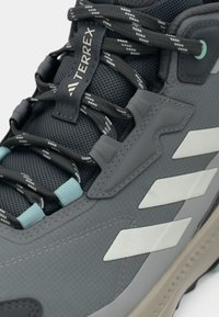 Γκρι αθλητικό παπούτσι με επάνω μέρος από δίχτυ, που διαθέτει ανοιχτό μπλε λεπτομέρειες, χοντρά κορδόνια και τρεις λευκές ρίγες στο πλάι.