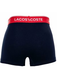 Boxer shorts in cotone blu navy con una cintura rossa a contrasto su cui è presente il testo "LACOSTE". Il design include una texture liscia e una vestibilità classica.