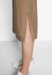 Beige knä-långa shorts med sidoventiler, tillverkade av mjukt tyg. Har en ren fåll och matchas med en ljusfärgad sneaker.