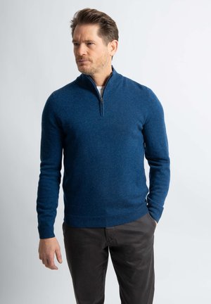 Marineblauwe trui met een ritskraag, gemaakt van zachte textuurstof, gecombineerd met donkerbruine broek, slank model en lange mouwen.