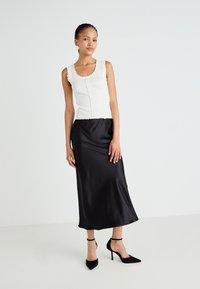 Haut sans manches blanc à bords ondulés, associé à une longue jupe en satin noire. Talons noirs à bout pointu avec des brides de cheville.