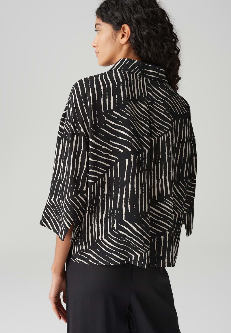 Czarna i biała marynarka w desenie, o luźnym kroju, szerokich rękawach i z kołnierzykiem, prezentująca odważną fakturę i wzór w paski.