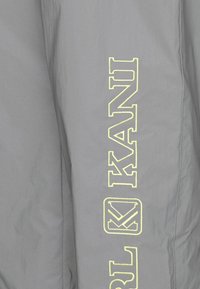 Grauer Stoff mit einer glatten Textur, der auf einer Seite in fetter gelber Stickerei den vertikalen Schriftzug "KANI" zeigt. Schlichtes Design.