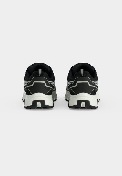 Paire de chaussures de sport noir et blanc vues de dos avec des semelles blanches épaisses et des détails réfléchissants sur fond blanc.