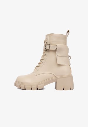 Simított bőrből készült bézs lépésre csatolt bokacsizma, robusztus sarkal, oldalsó csattal és fedélzseb részletekkel. Texturált talp a tapadás érdekében.