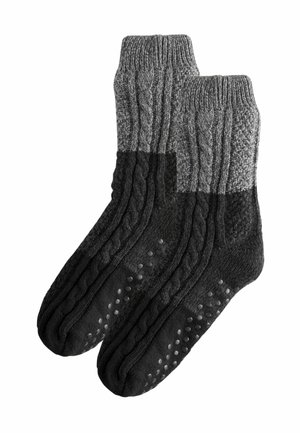 Gestrickte Socken in Grau mit schwarzen Akzenten, die ein Kabelmuster aufweisen und über Anti-Rutsch-Punkte an der Sohle für besseren Halt verfügen.