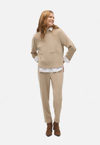 Suéter beige con cuello redondo y un acabado texturizado, combinado con pantalones tapered a juego. Botines de tacón marrones completan el conjunto.