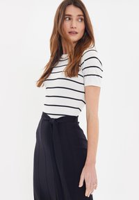 Maglione a righe bianco e nero, con colletto rotondo e maniche corte, abbinato a pantaloni neri a vita alta con cintura annodata.