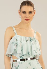 Top floreale azzurro chiaro con sovrapposizione arricciata, spalline sottili e un'accattivante cintura argentata in vita. Tessuto morbido e leggero con stampe botaniche.