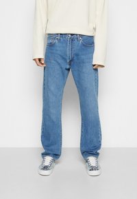 Ljusblå raka jeans i denim, med klassisk femficksdesign och knäppning med övre knapp. Bärs med en ribbad vit tröja.