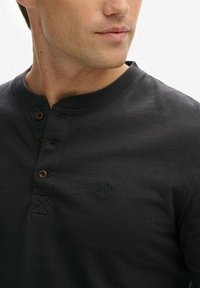 Czarna bawełniana koszula henley z okrągłym dekoltem, trzema guzikami, małym haftowanym logo i minimalnymi detalami szycia.