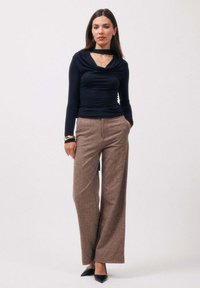 Haut bleu marine à manches longues avec un col bénitier, associé à un pantalon marron à jambes larges. Talons noirs à bout pointu et bracelets dorés complètent le look.