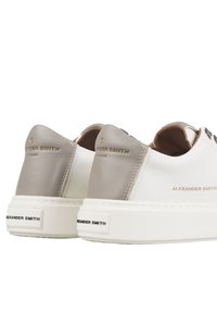 Sneaker in pelle bianca con accenti grigi, caratterizzate da una superficie liscia, tappi sul tallone a contrasto e dettagli con logo dorato sul retro.