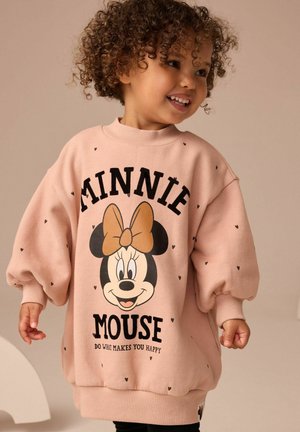 Jeune enfant souriant aux cheveux bouclés portant un pull rose oversize avec Minnie Mouse et le texte "Do what makes you happy."