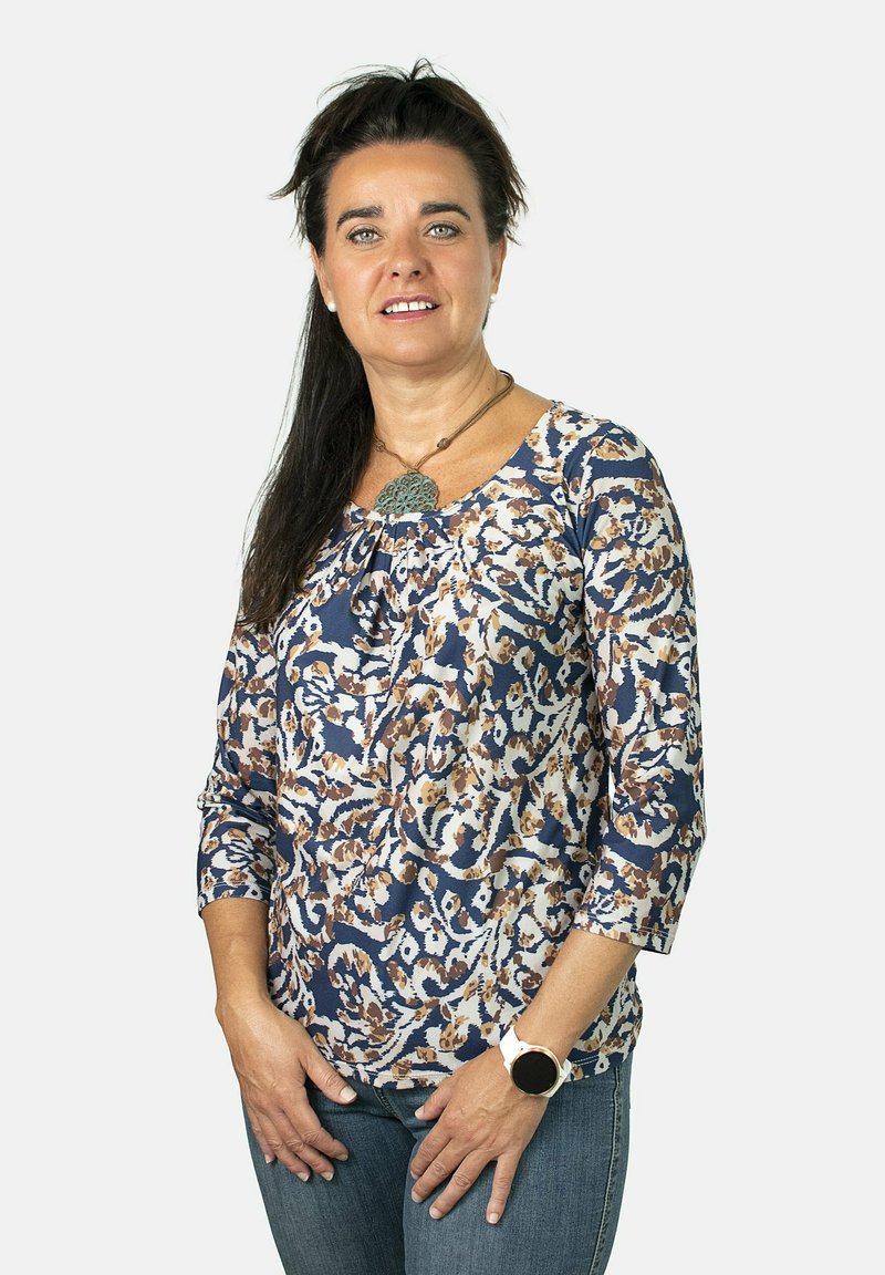 Top de color azul marino y crema con estampado, mangas de tres cuartos y escote redondo; fabricado en tela suave; combinado con jeans y un reloj de pulsera.