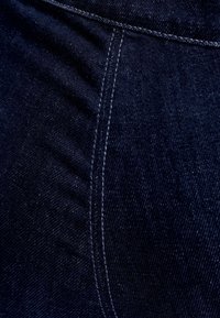 Tumma sininen farkkukangas, jossa on sileä pinta, näkyvät ompeleet reunoilla ja hienovaraiset vaihtelut kudontamallissa.