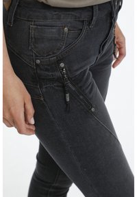 Jean en denim noir à coupe ajustée, avec une poche zippée, des coutures contrastantes et un détail en tissu texturé.