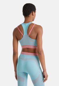 Lichtblauwe sportbeha en leggings met roze accenten. Bevat een geometrisch patroon en contrasterende banden, gemaakt van rekbaar materiaal.