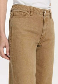 Beige denim jeans met een hoge taille, voorzien van een ritssluiting, voorzakken en een iets losse pasvorm. De textuur is glad met een subtiele glans.