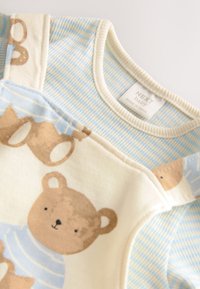 Ensemble pour bébé en coton, bleu clair et crème. Présente une texture rayée, un motif d'ours et une fermeture à pression sur l'épaule. Étiquette "NEXT baby" visible.
