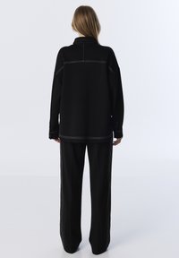 Czarny, oversize'owy sweatshirt z białymi detalami w szwach, zestawiony z szerokimi czarnymi spodniami z bocznymi pasami. Prosty, funkcjonalny design.