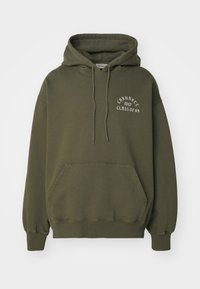Ciemnooliwkowy sweatshirt z kieszenią z przodu, kapturem ze sznurkiem i białym napisem "CARHARTT KLASA 89" na klatce piersiowej. Miękki, polarowy materiał.