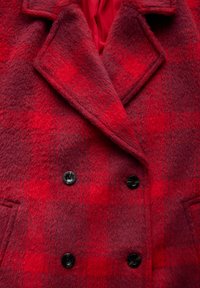 Red plaid double-breasted coat made of textured fabric, featuring large black buttons, pronounced lapels, and a smooth inner lining.