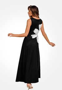 Vestido maxi negro con un diseño sin mangas, que presenta un gran patrón floral blanco en la parte posterior y una silueta suelta y fluida.