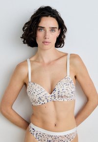 Bra with a light beige base, featuring a subtle brown and blue speckled pattern. Thin, white adjustable straps and a smooth texture.