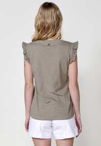 Camiseta verde oliva con mangas cortas de encaje, escote redondo y corte relajado, combinada con pantalones cortos blancos.