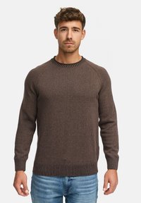 Pull en maille marron avec un col et un ourlet côtelés, présentant un tissage texturé et des manches raglan. Porté avec un jean en denim bleu.